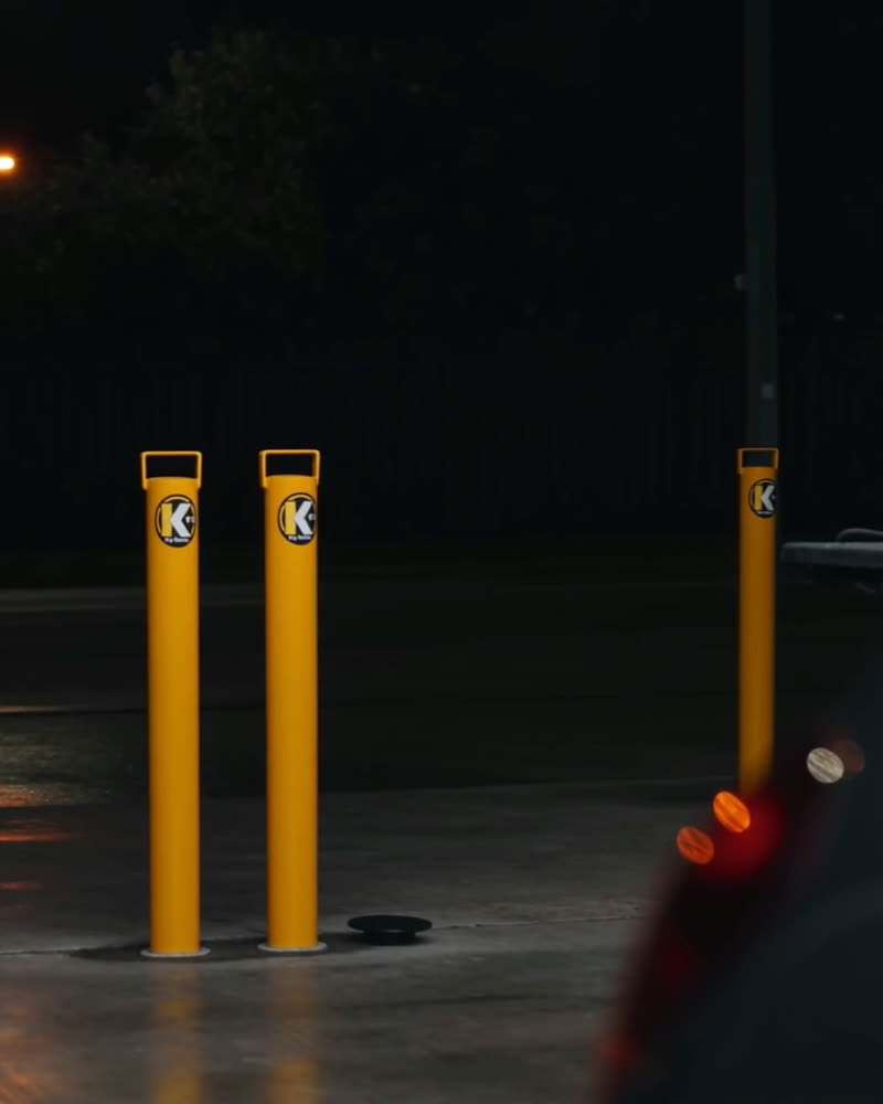 Three yellow Key Bollards with K badges guarding a home garage forecourt at night, a flush cap fitted in the fourth socket and a car parked alongside