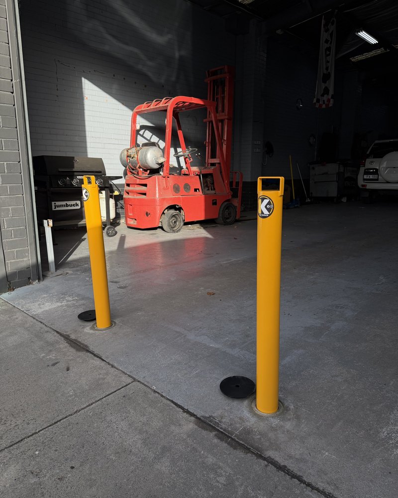 Two yellow Key Bollards protecting a Melbourne warehouse entrance with a forklift working inside